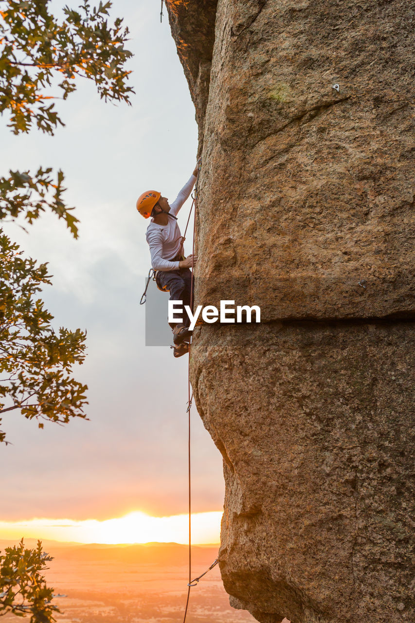 Male mountaineer climbing high cliff with safety carabiner and ropes