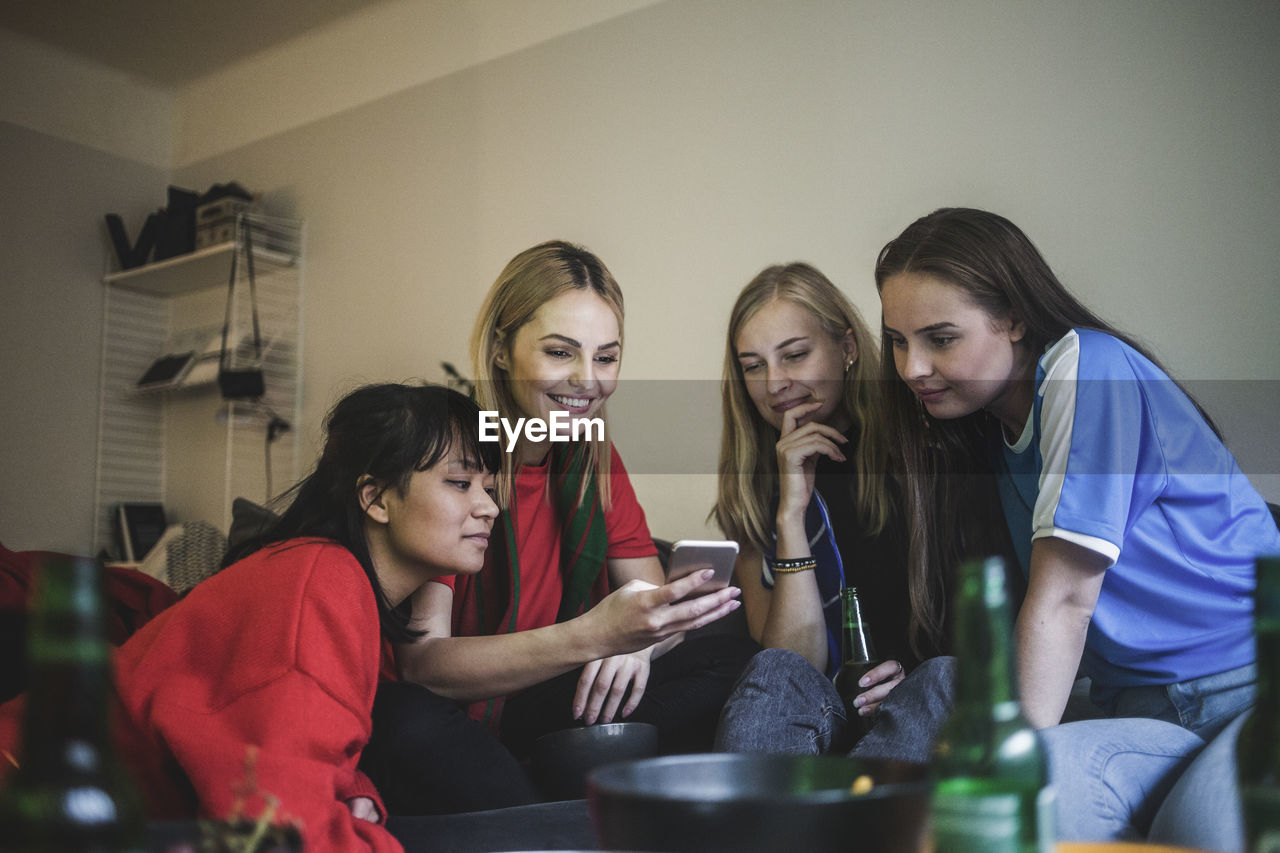 Smiling female friends using mobile phone while sitting at home