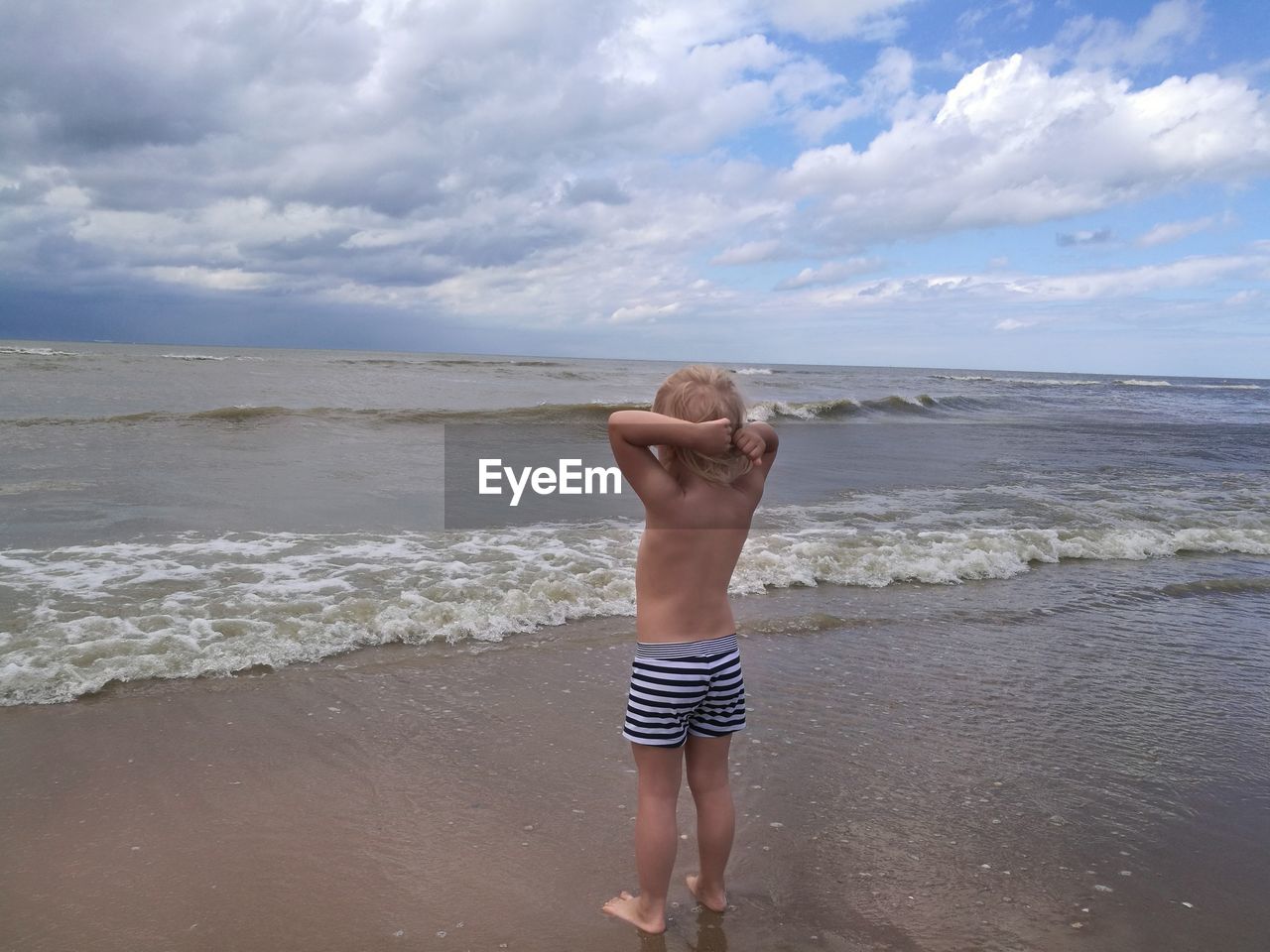 Full length of shirtless boy standing on beach against sky