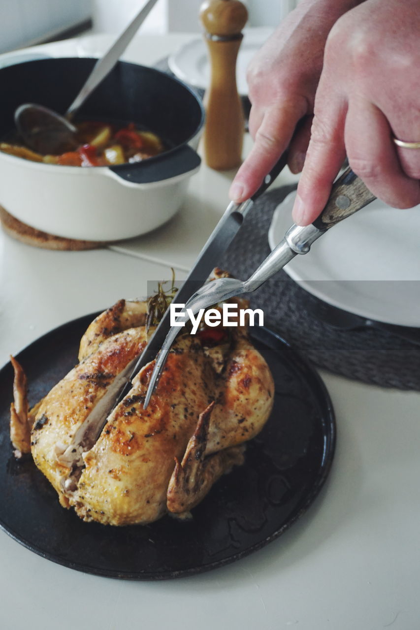 Cropped hand of woman cutting roasted chicken in plate