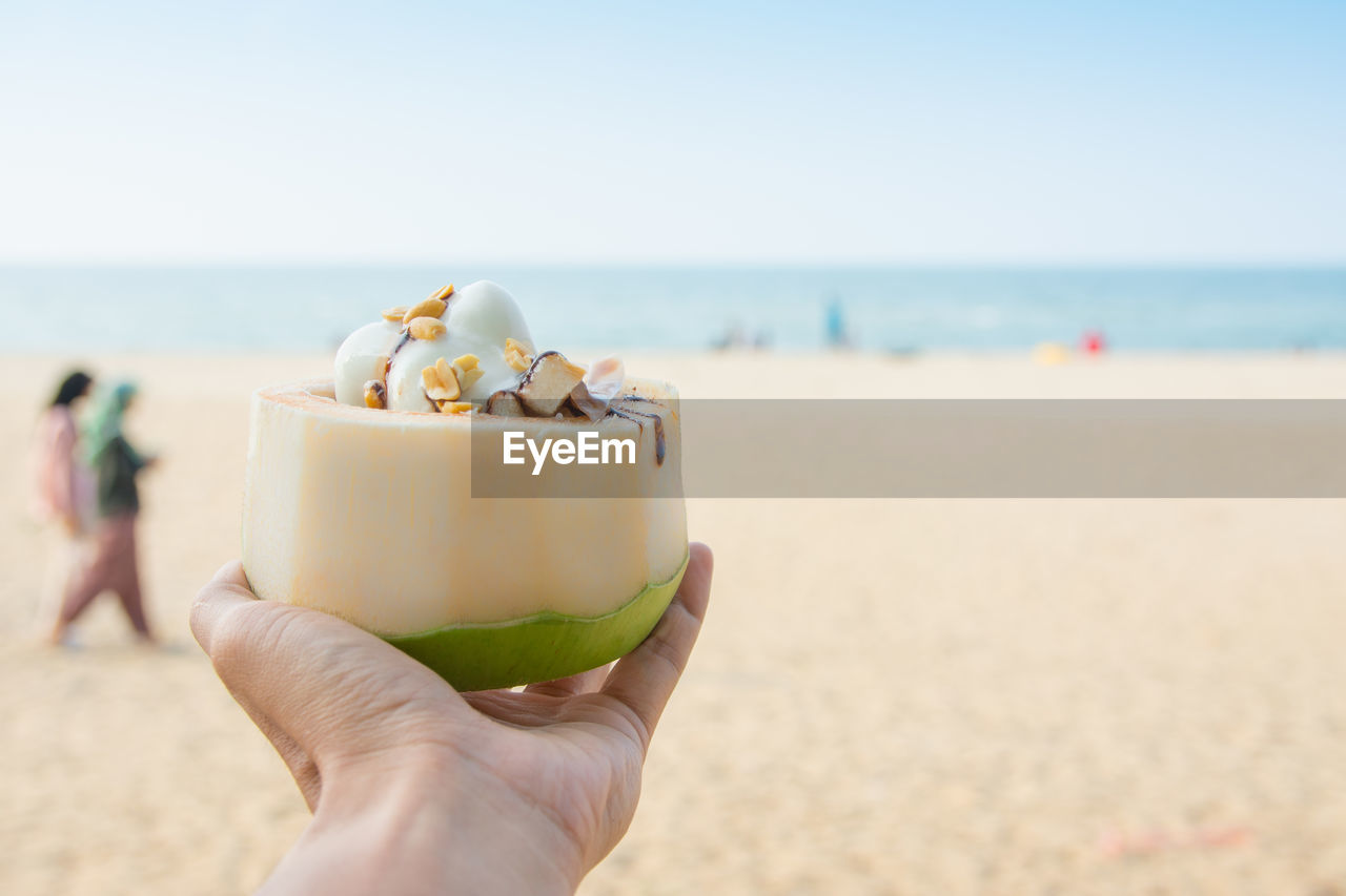 CROPPED IMAGE OF HAND HOLDING ICE CREAM ON BEACH