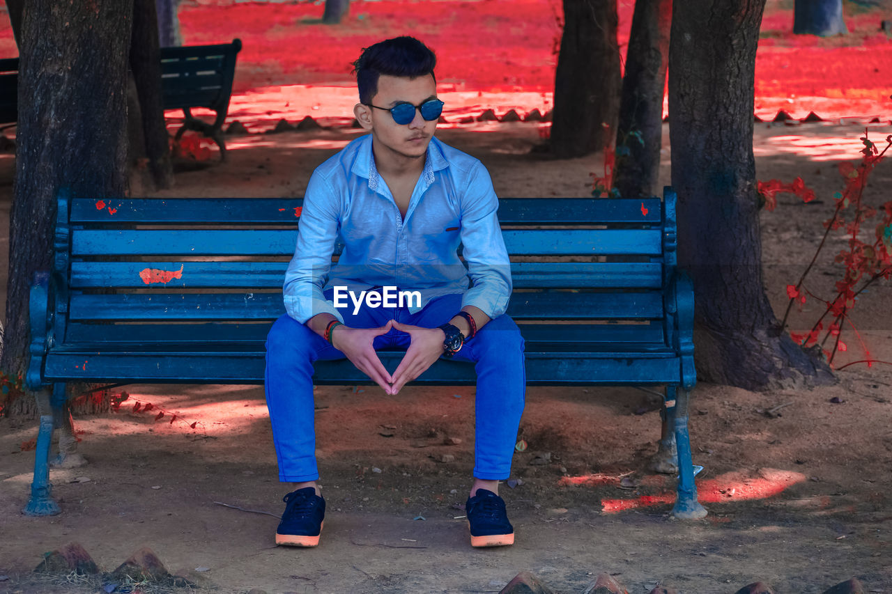 blue, one person, sitting, red, full length, bench, front view, seat, men, adult, young adult, relaxation, casual clothing, person, lifestyles, fashion, portrait, leisure activity, clothing, spring, glasses, furniture, architecture, outdoors, serious, electric blue, city, nature, looking at camera