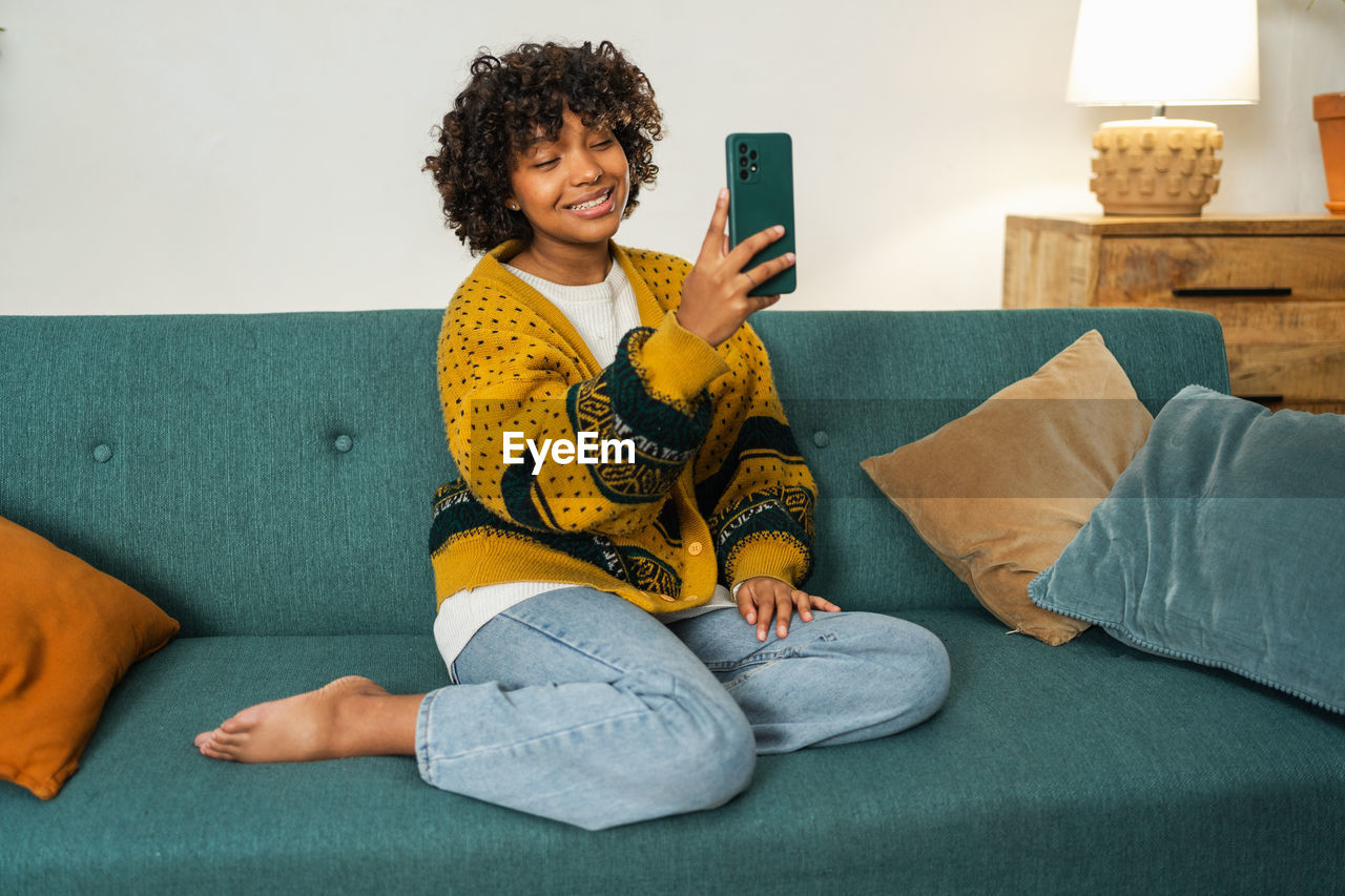 portrait of young woman using mobile phone while sitting on sofa at home