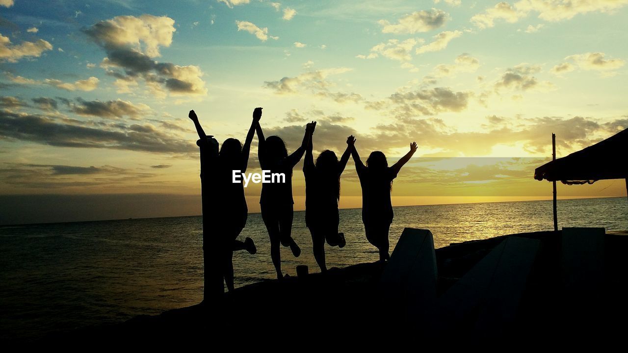 Silhouette female friends dancing at beach against sky during sunset