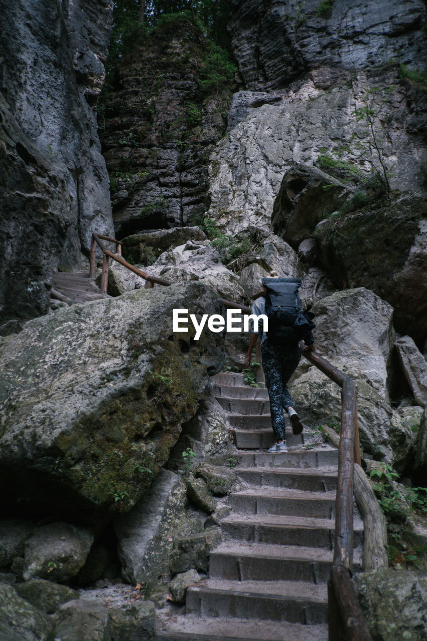 Low angle view of hiker with backpack moving up on steps towards rock formations