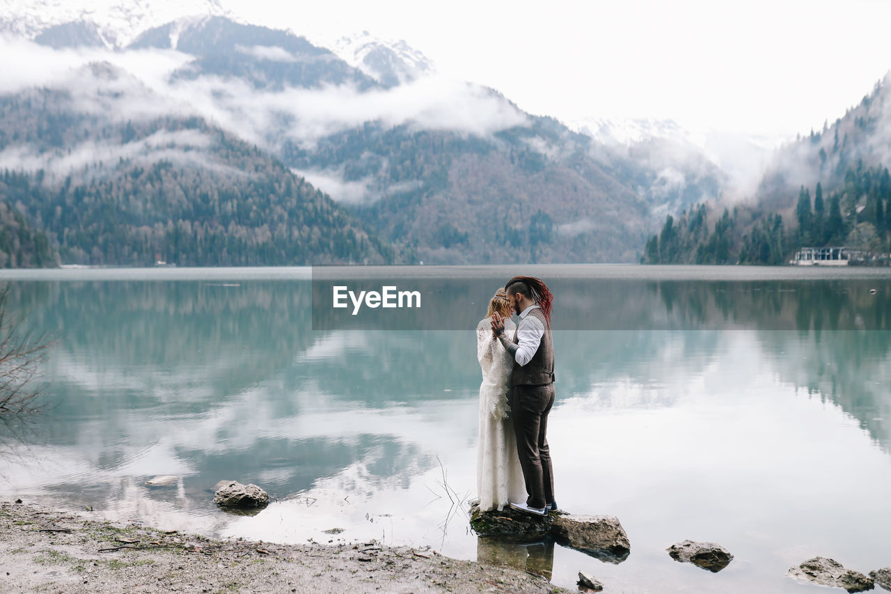 Happy newlyweds in love a man and a woman in wedding clothes embrace on the shore of the lake