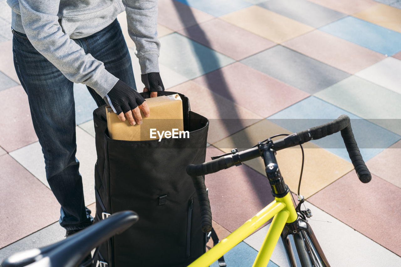 Delivery man removing package from backpack by bicycle on footpath