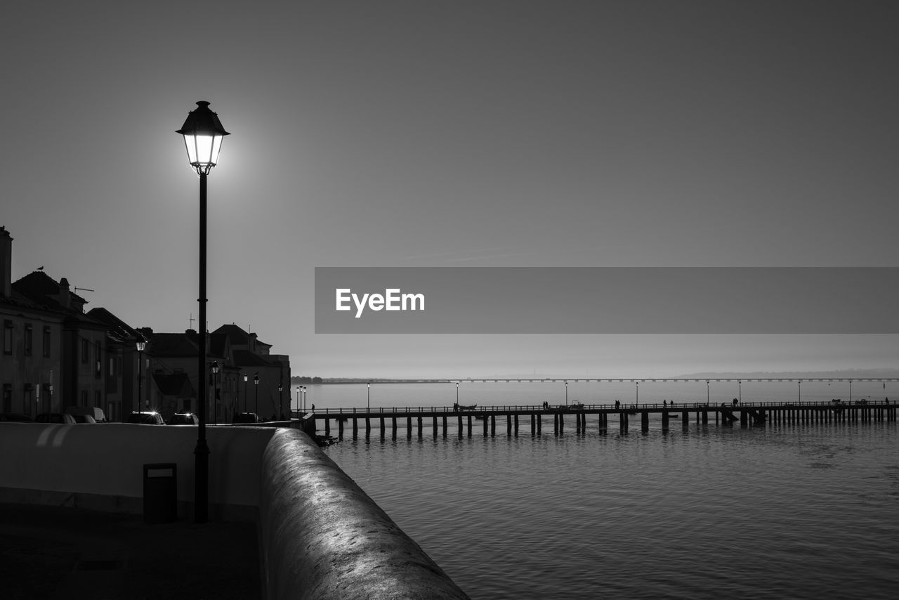 Illuminated street light by sea against sky