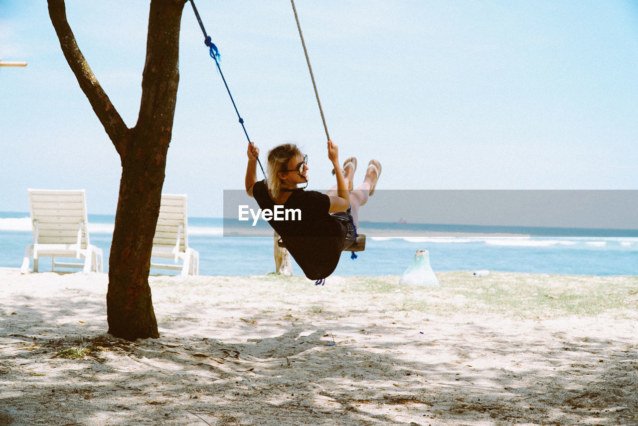 Rear view of woman on swing at beach