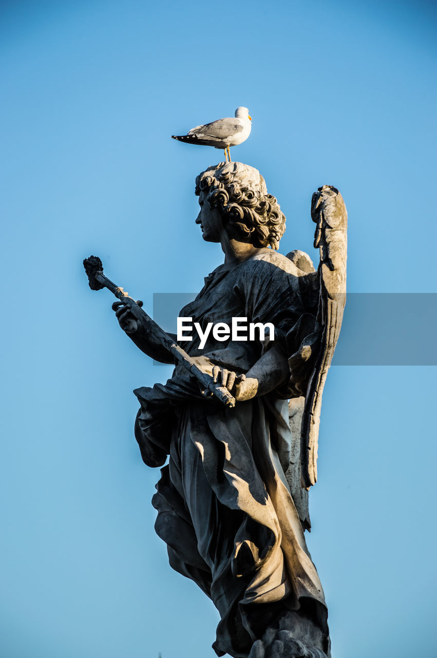 Bird perching on statue against clear blue sky