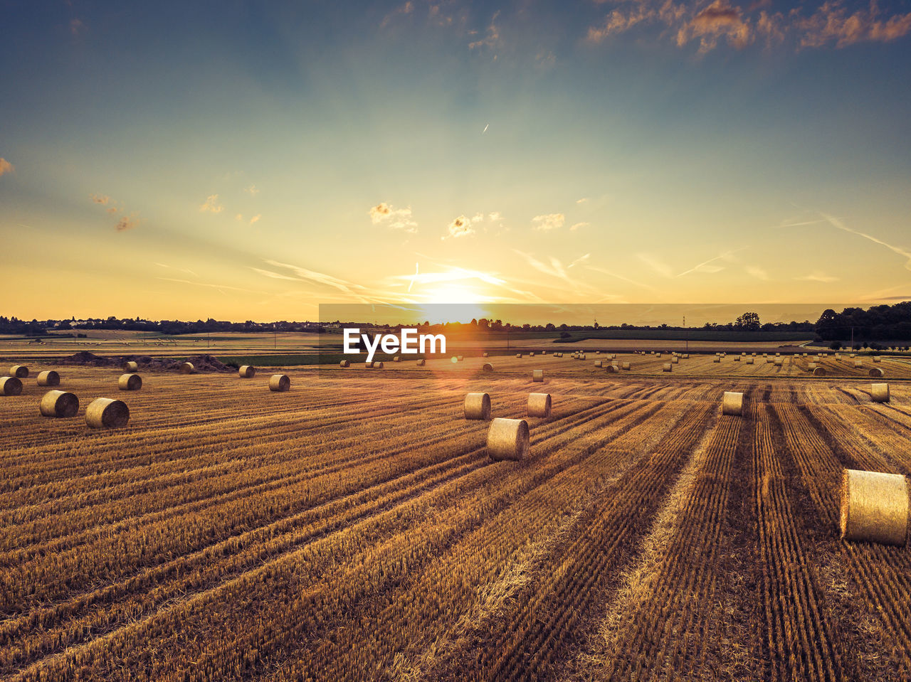 Hay bales on field against sky during sunset