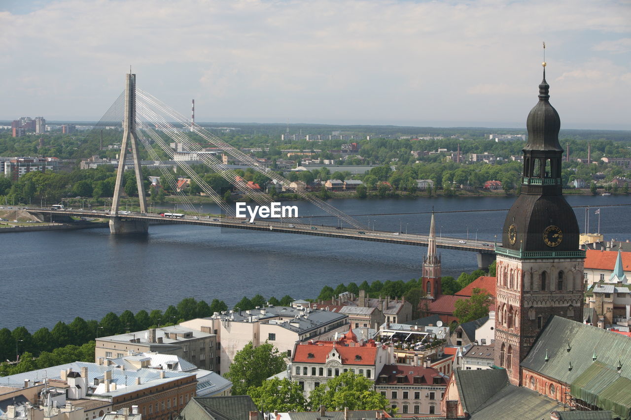 Buildings by bridge and river against sky on sunny day