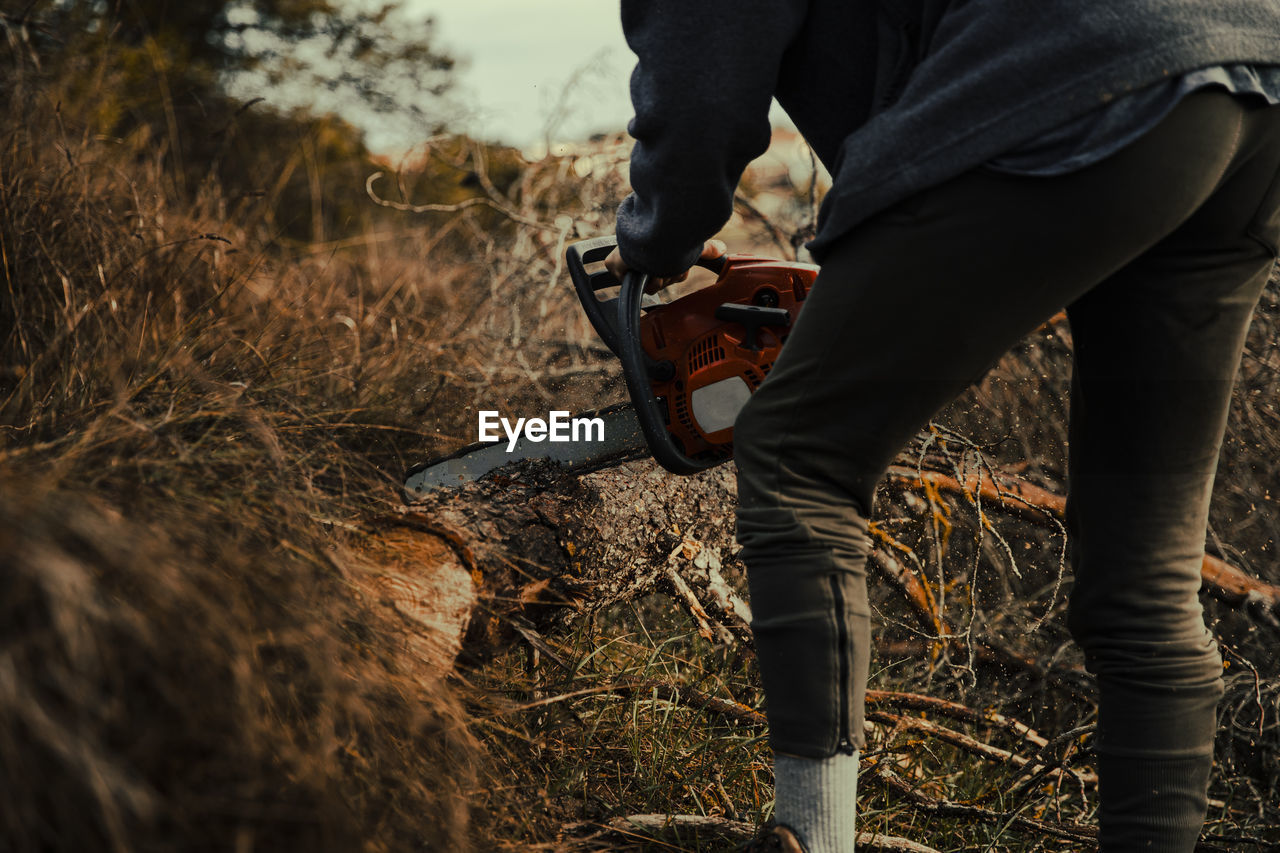 Teenage boy cutting wood with chainsaw in forest