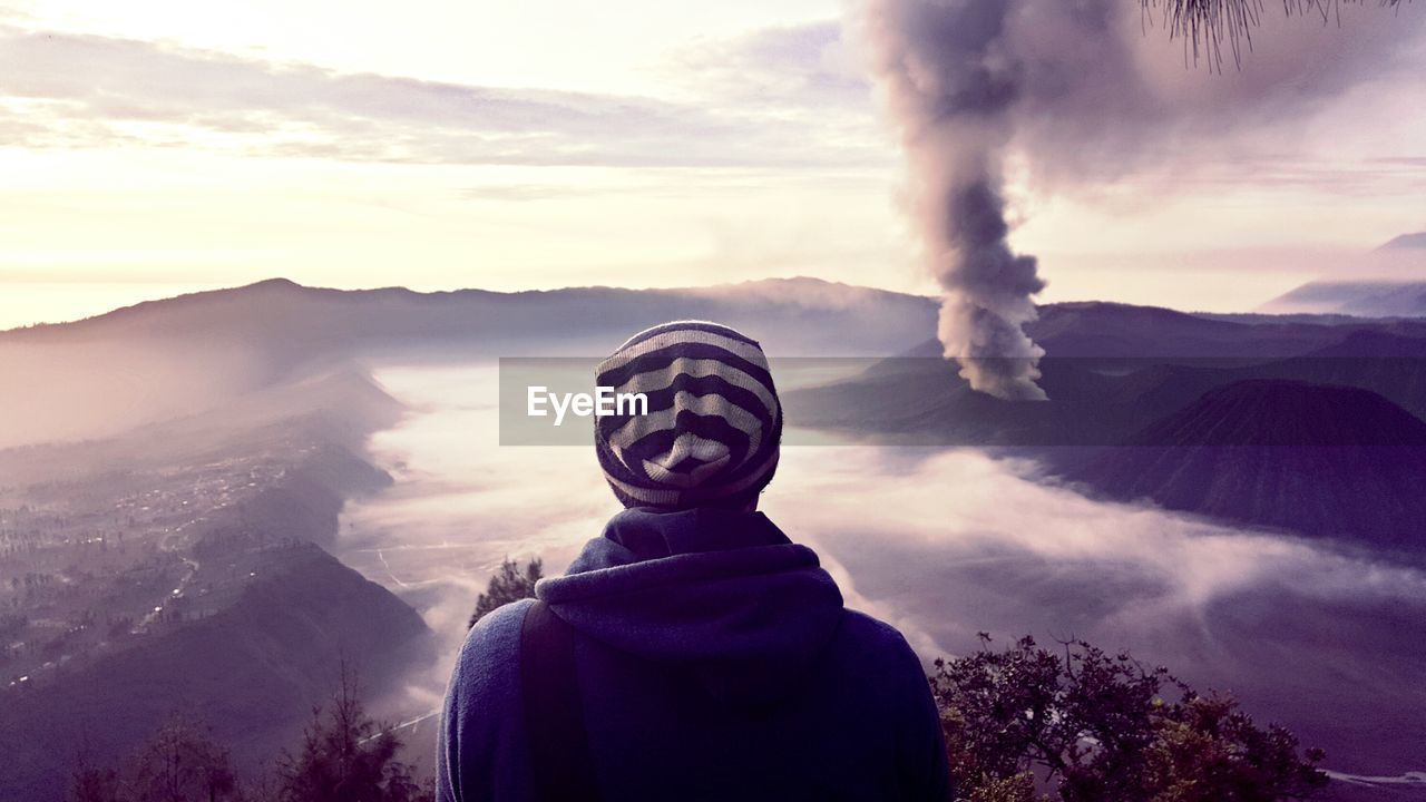 Rear view of person by volcano against sky during sunset