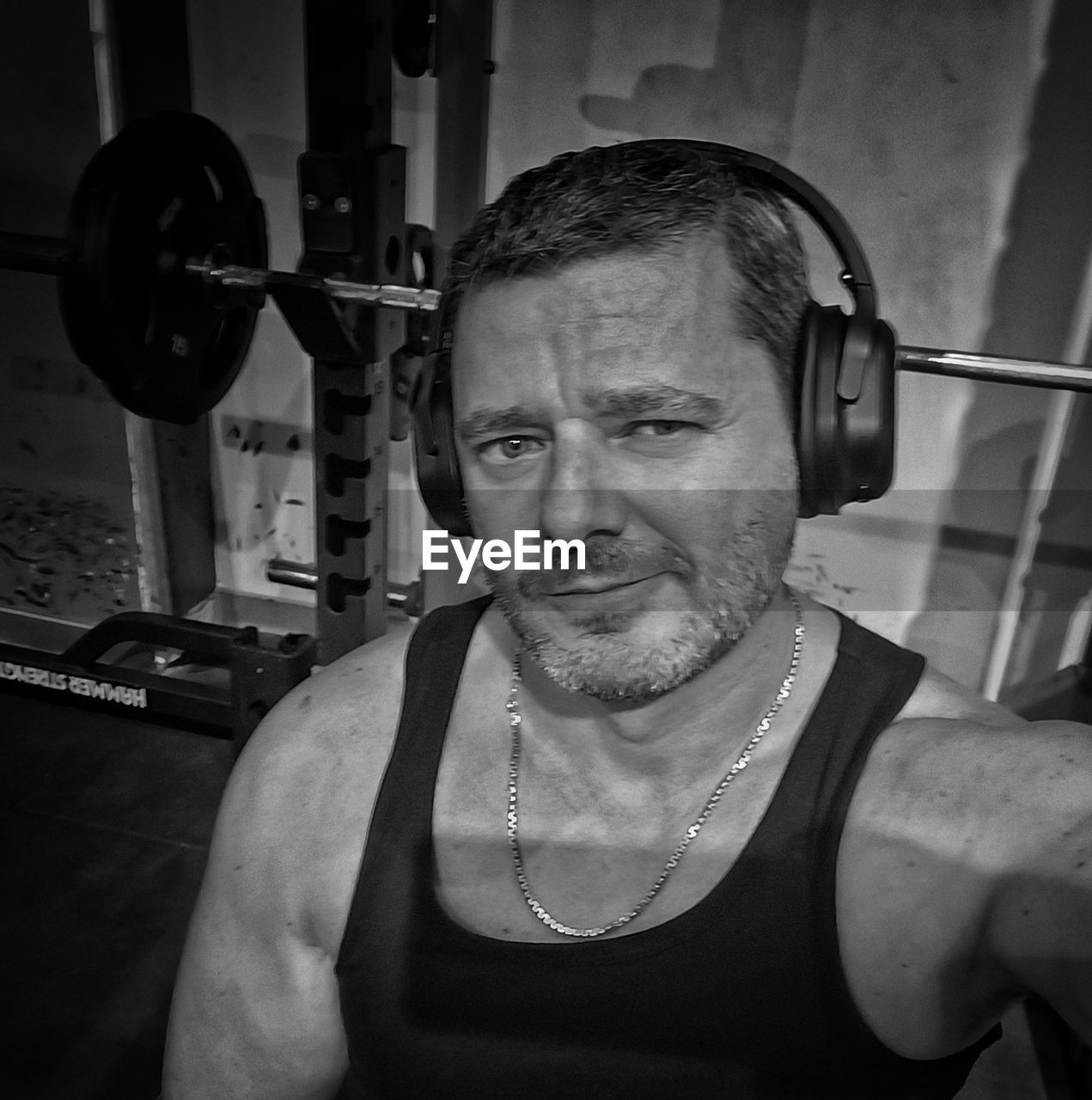bodybuilding, adult, one person, exercising, sports training, strength, muscular build, gym, lifestyles, sports, weight, men, weight training, portrait, mature adult, indoors, black and white, front view, arm, health club, vitality, barbell, athlete, person, equipment, determination, monochrome, waist up, leisure activity, black, sport venue, sports equipment, physical fitness, wellbeing, monochrome photography, room, tank top