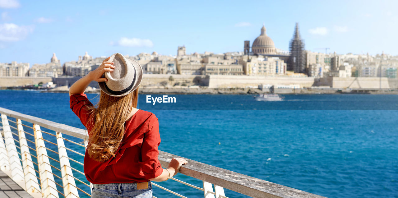 Panoramic view of female tourist holding hat looking at the city of valletta, malta.