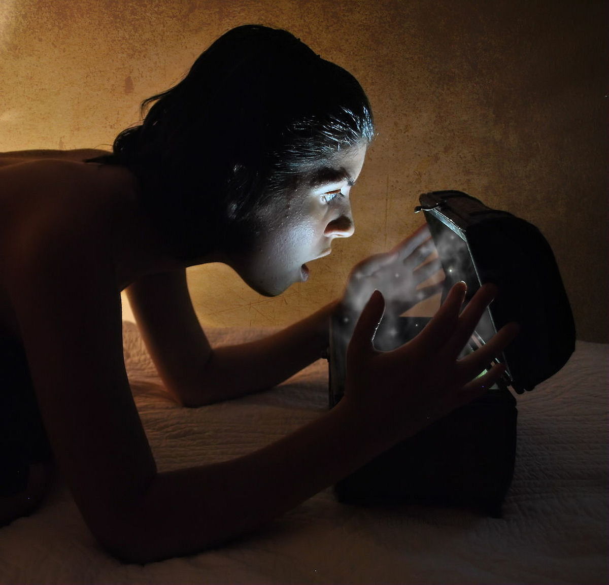 Side view of surprised woman looking in illuminated box on bed against wall