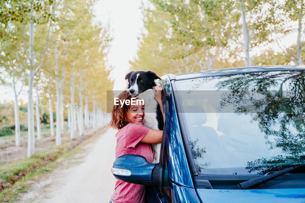 Side view of woman embracing dog through car window