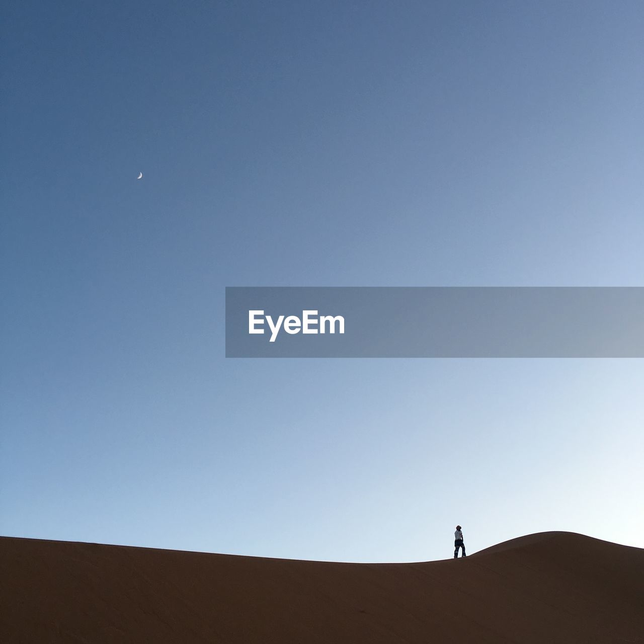 MAN STANDING IN DESERT AGAINST CLEAR SKY