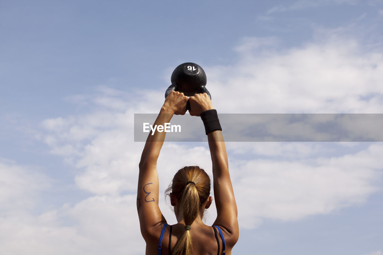 REAR VIEW OF WOMAN WITH ARMS OUTSTRETCHED AGAINST CLOUDY SKY