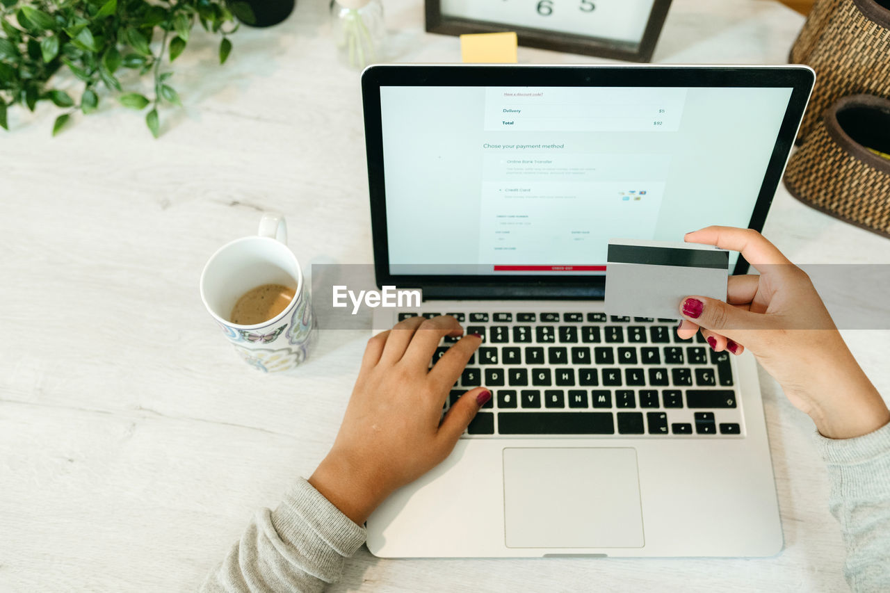 Crop unrecognizable female making purchase with plastic card for order during online shopping via laptop