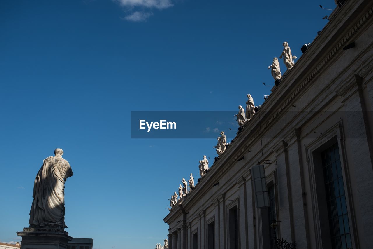 Low angle view of statue by st peter basilica against sky