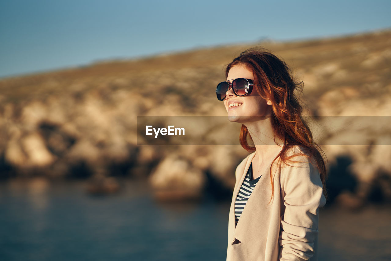 PORTRAIT OF SMILING YOUNG WOMAN WEARING SUNGLASSES