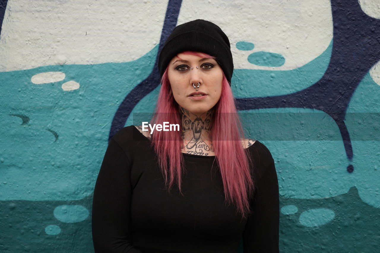 Portrait of smiling woman with pink hair standing against graffiti wall