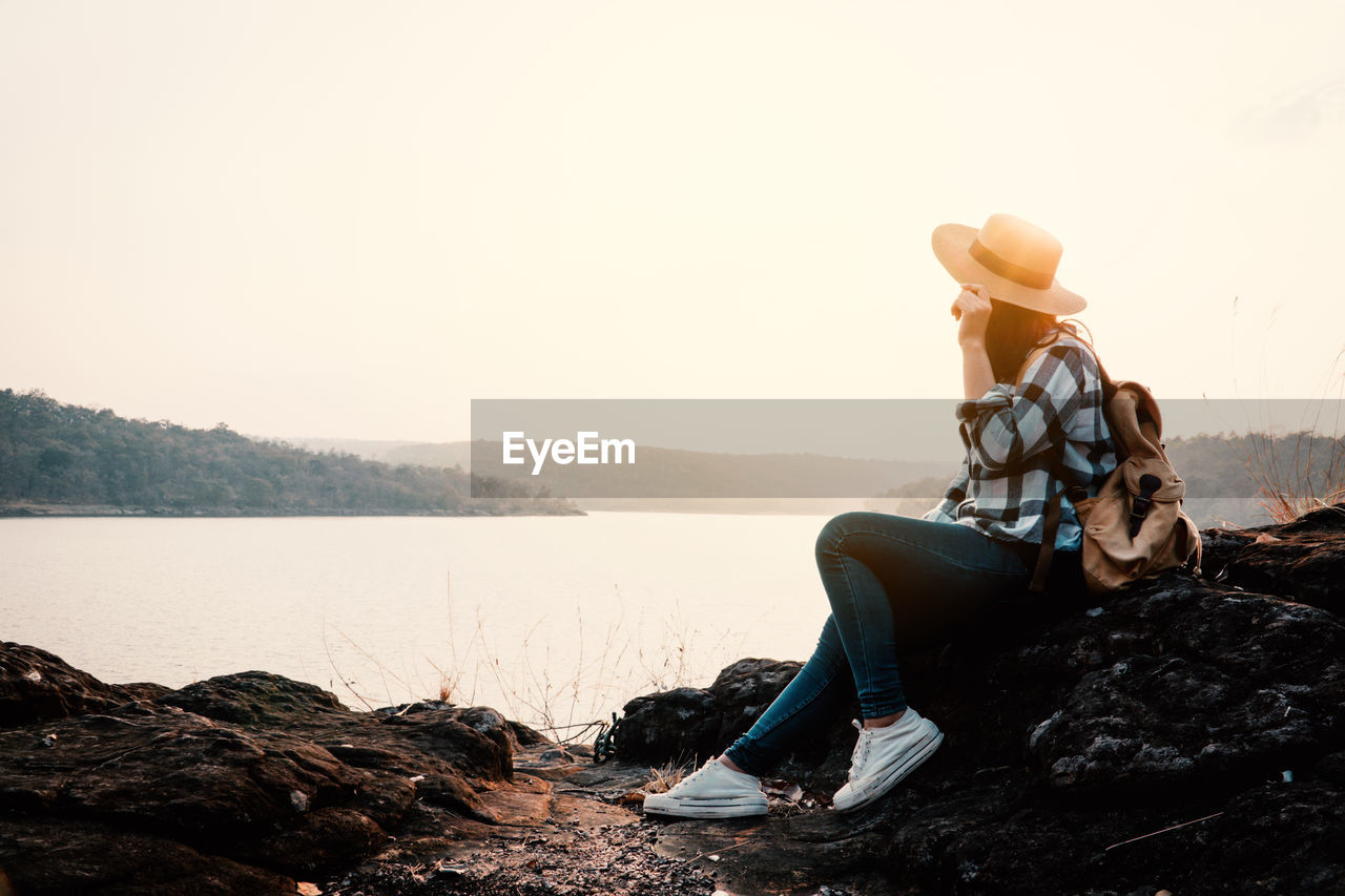 Woman sitting on rock looking at view of lake against sky