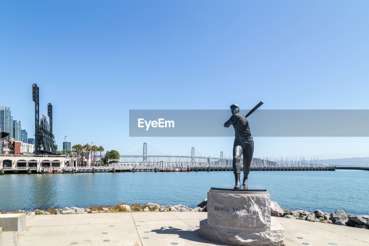 MAN STANDING BY SEA AGAINST CLEAR SKY