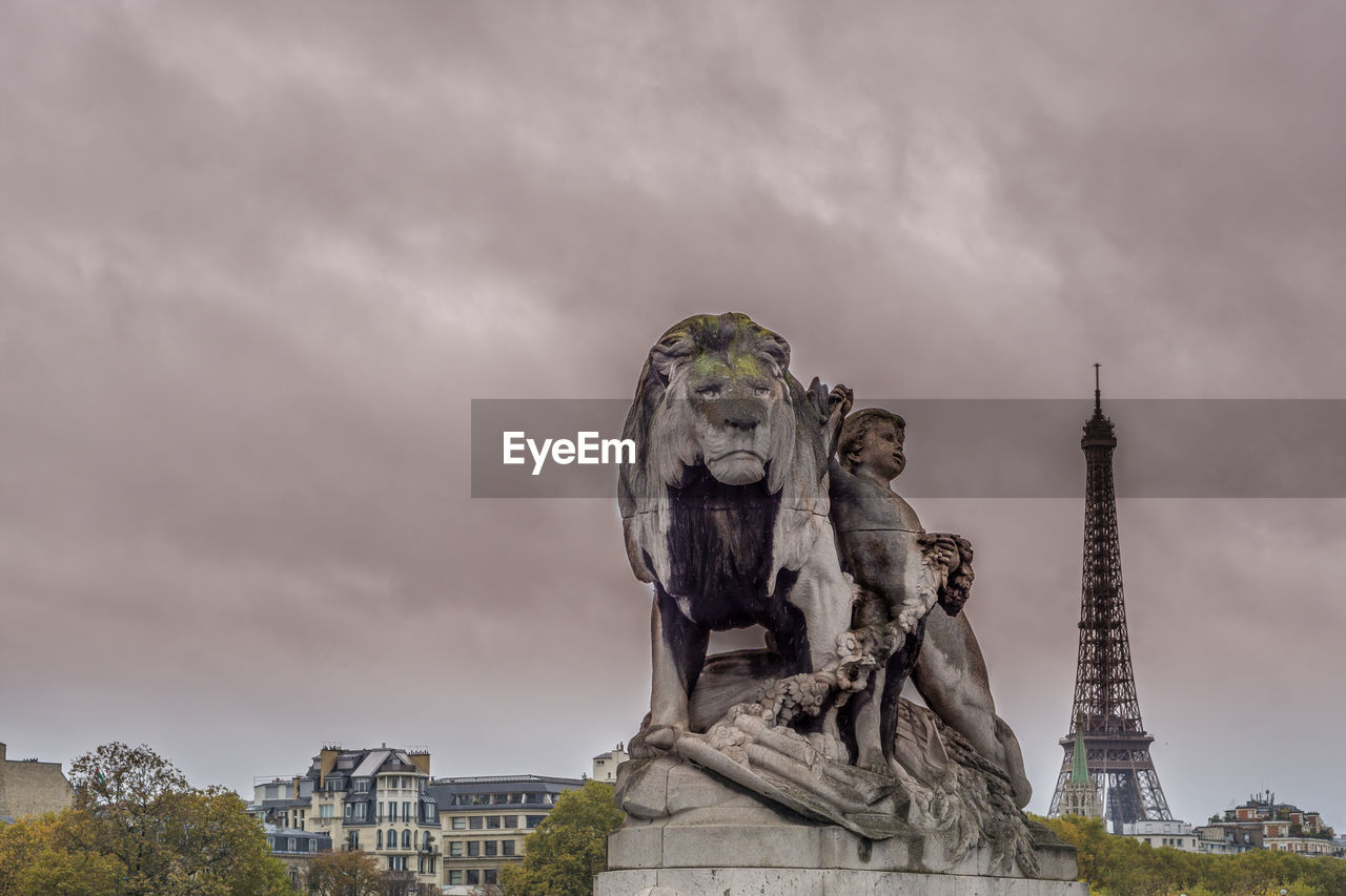 LOW ANGLE VIEW OF STATUE IN CITY AGAINST CLOUDY SKY