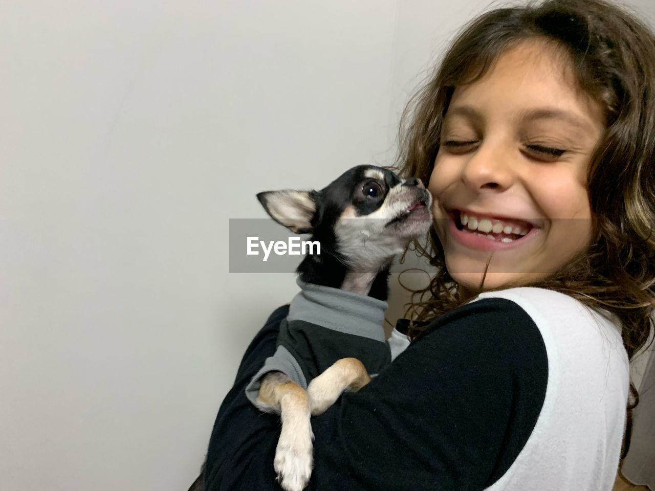 Side view of happy girl carrying cute dog while standing against wall