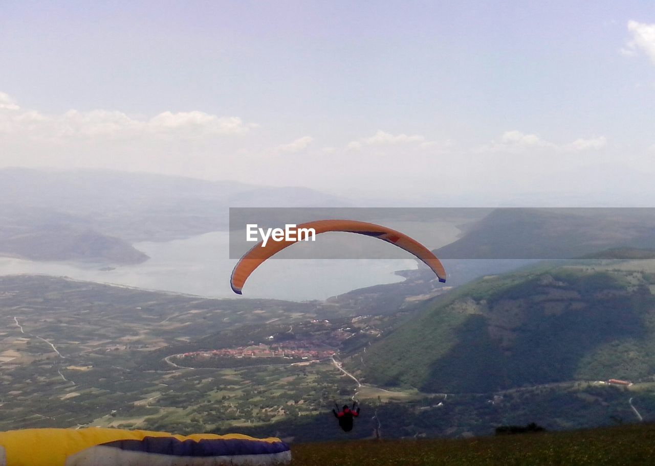 MAN PARAGLIDING OVER MOUNTAIN AGAINST SKY