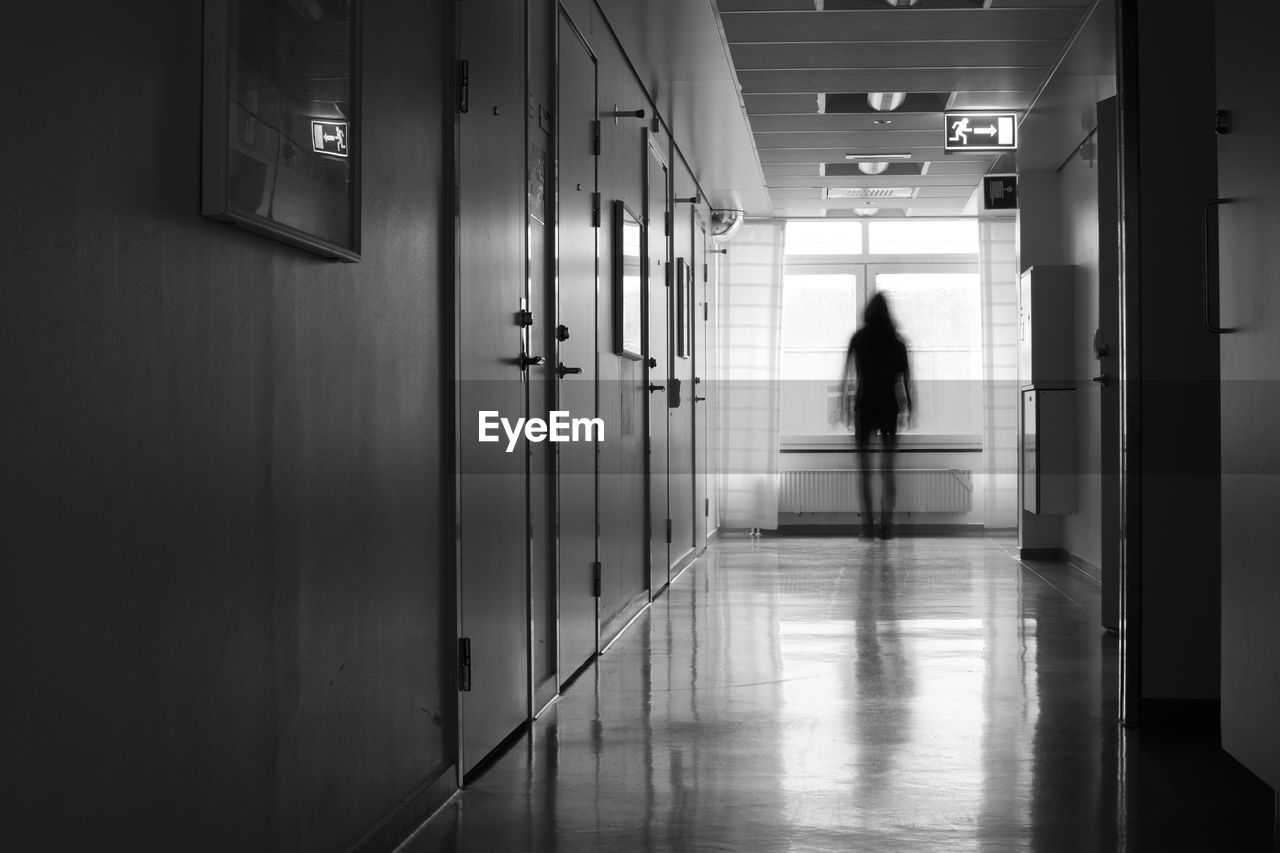 REAR VIEW OF MAN WALKING IN BUILDING CORRIDOR