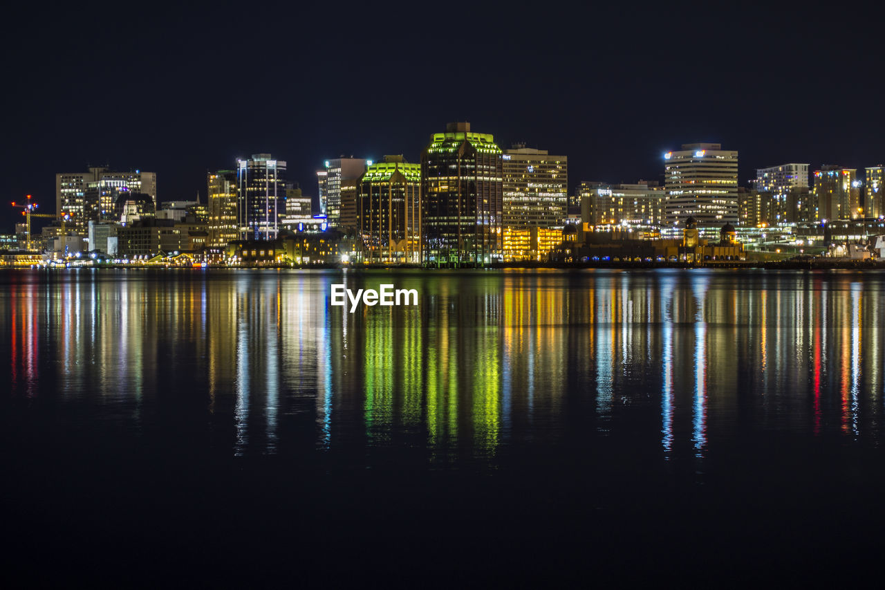 Illuminated buildings by river against sky at night