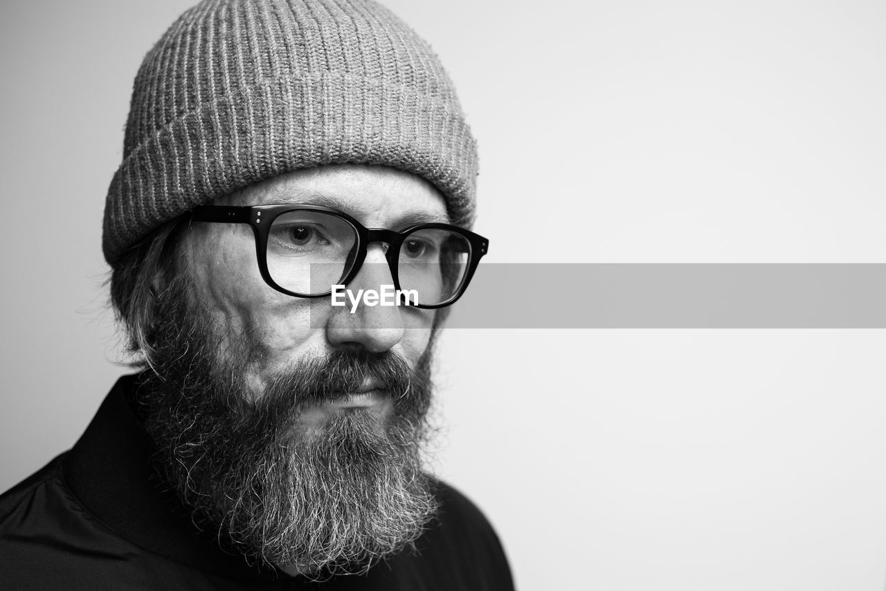 Close-up of man wearing knit hat while looking away against white background