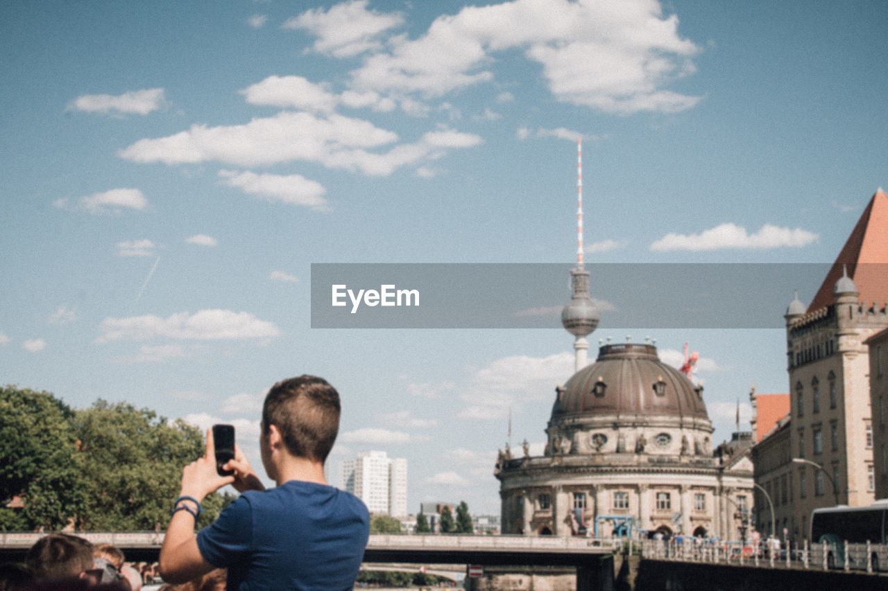 Rear view of man photographing in city with fernsehturm in background