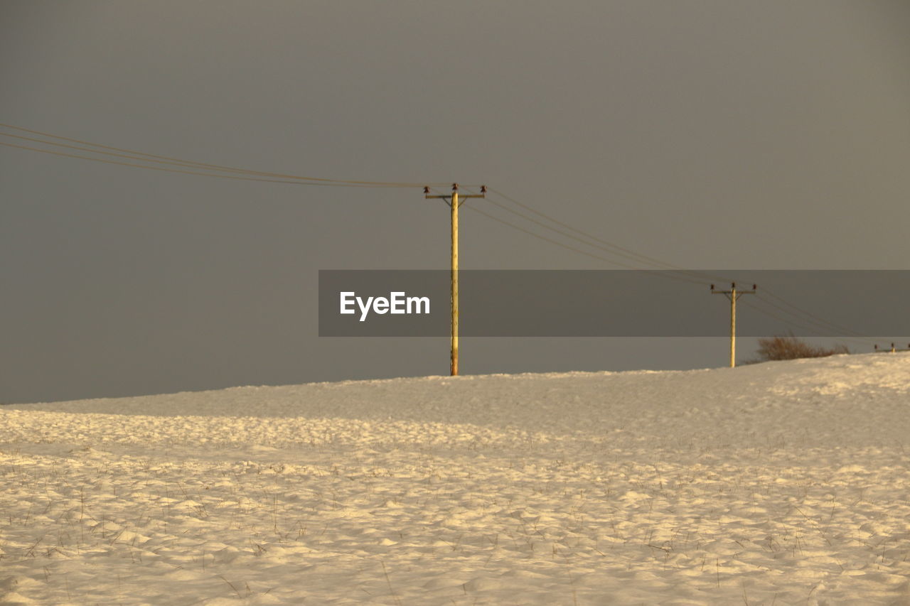 Electricity pylon on snow covered land against clear sky