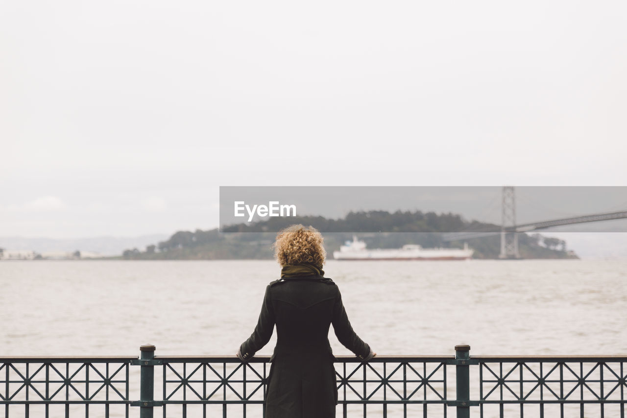 Rear view of woman standing by railing on pier over sea against sky