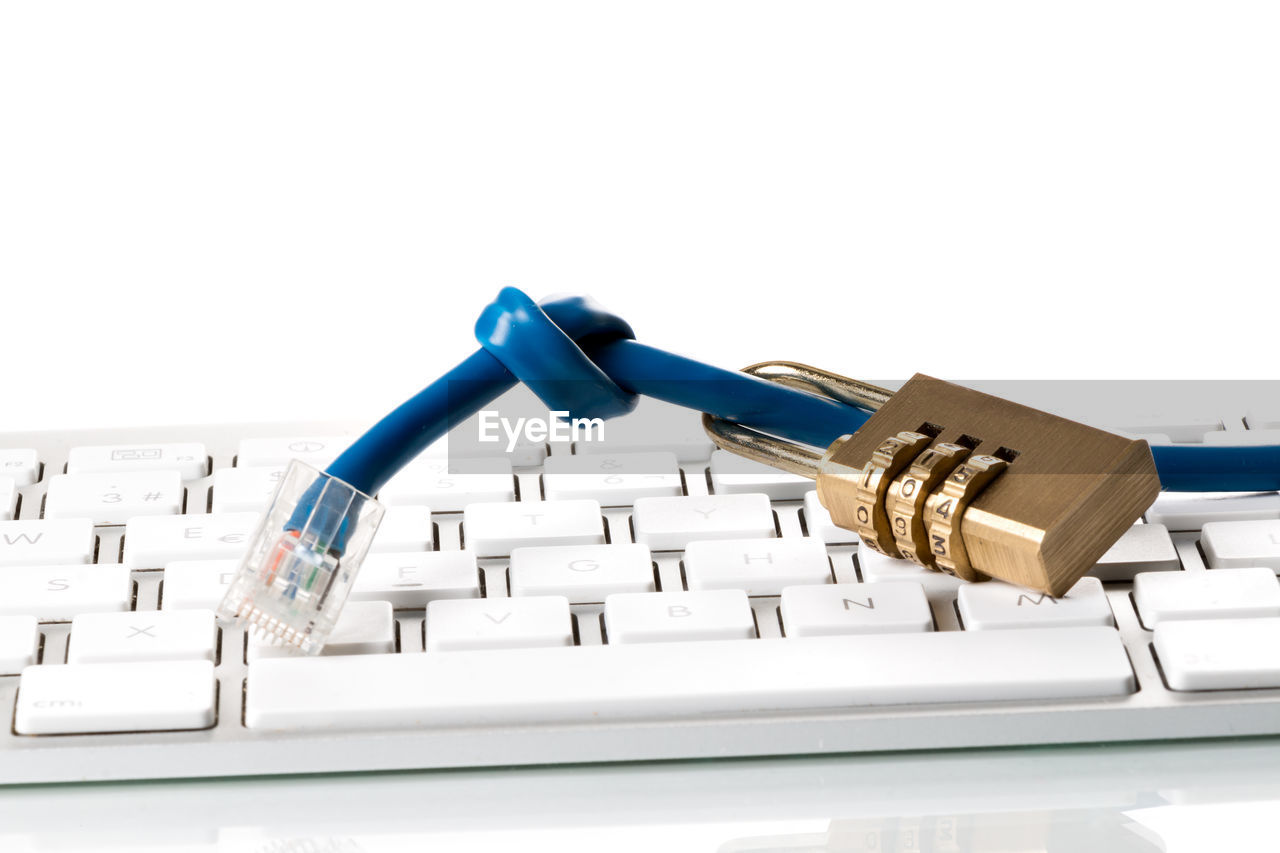 Close-up of padlock and cable on computer keyboard against white background