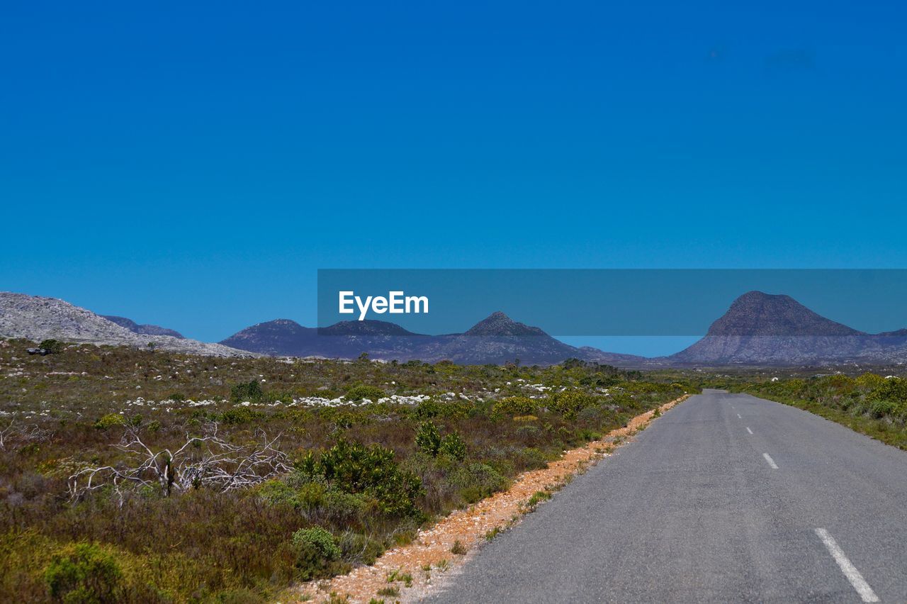 ROAD BY MOUNTAINS AGAINST BLUE SKY