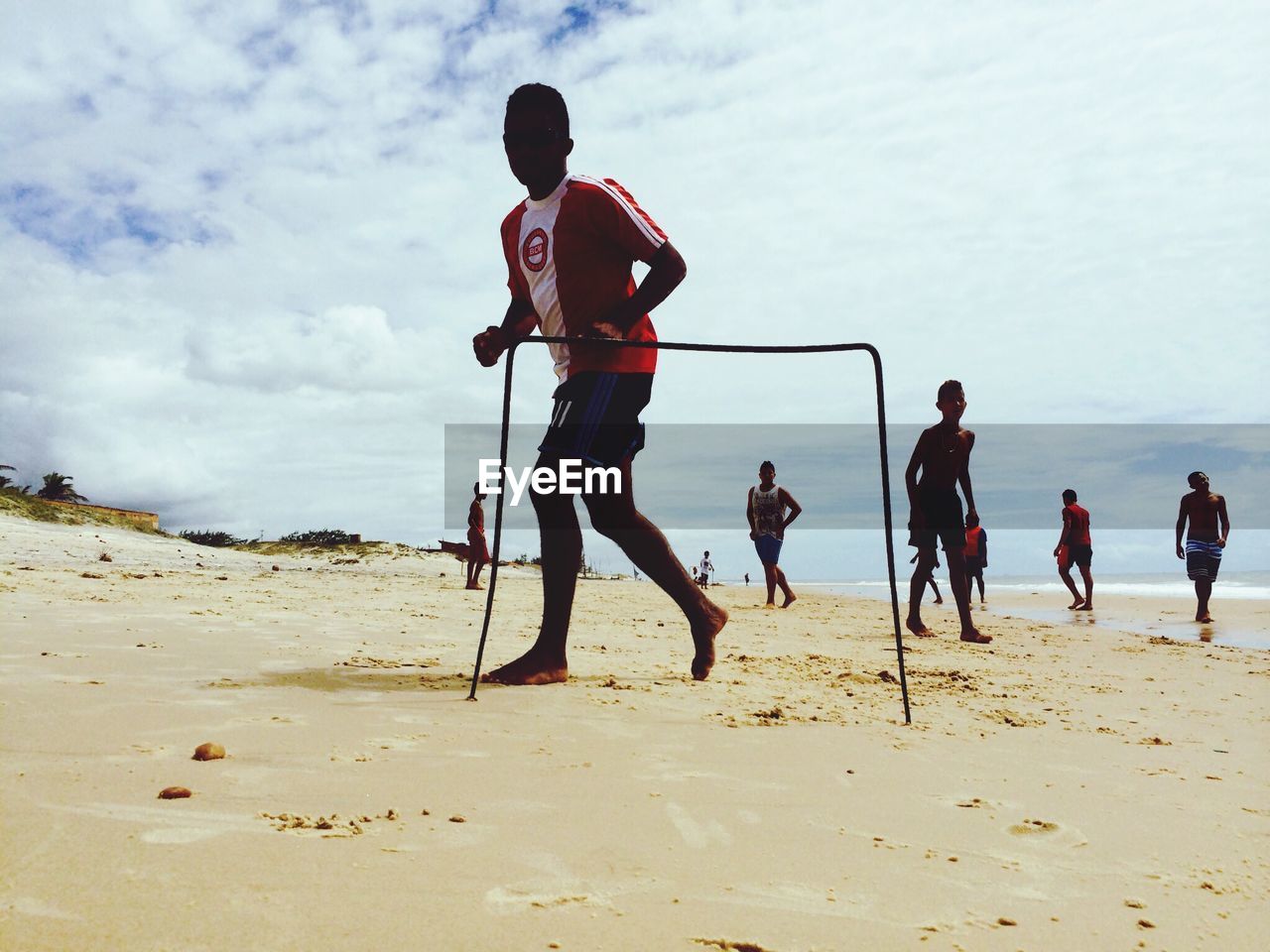 Men playing football on beach against cloudy sky