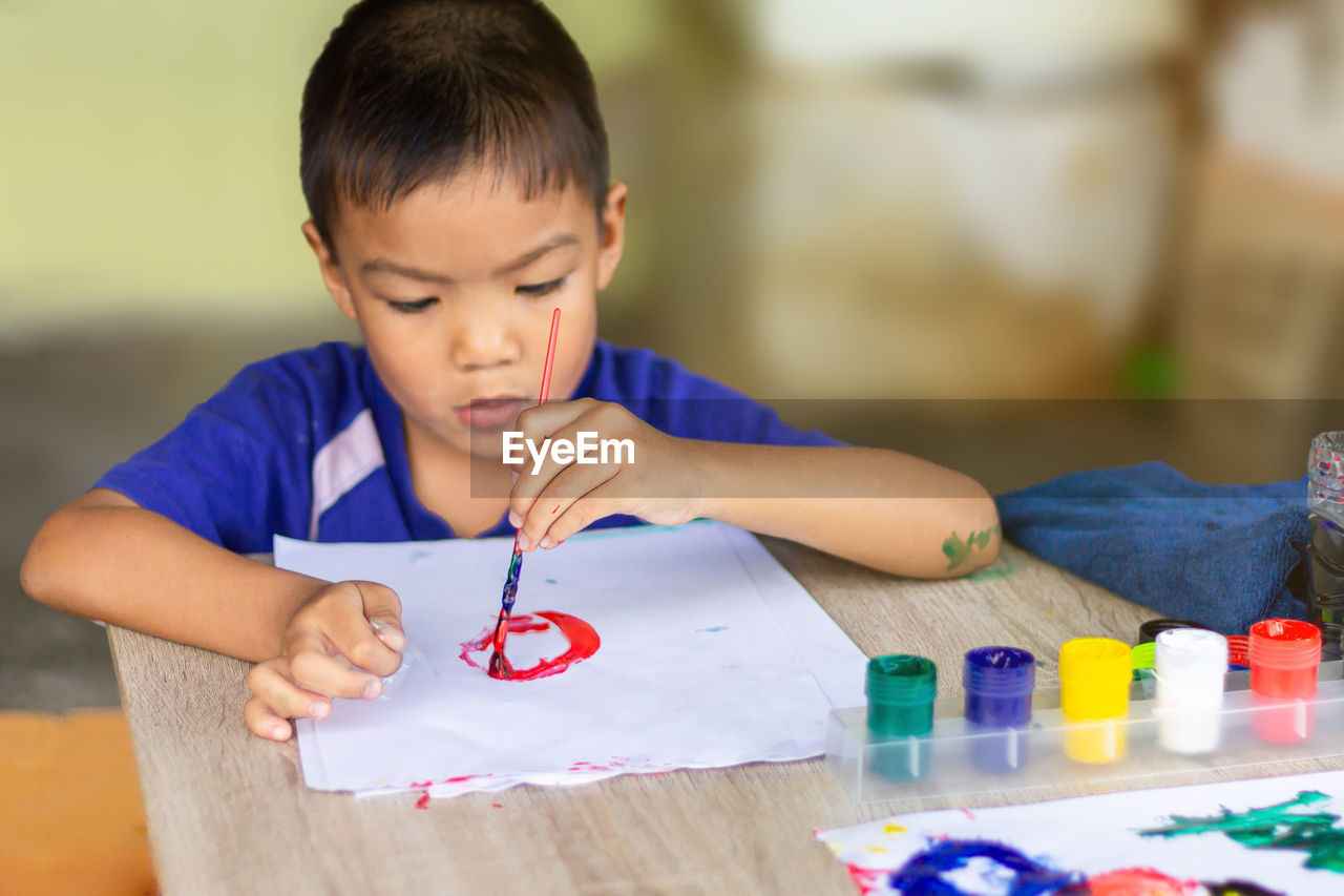 Cute boy painting while sitting on table