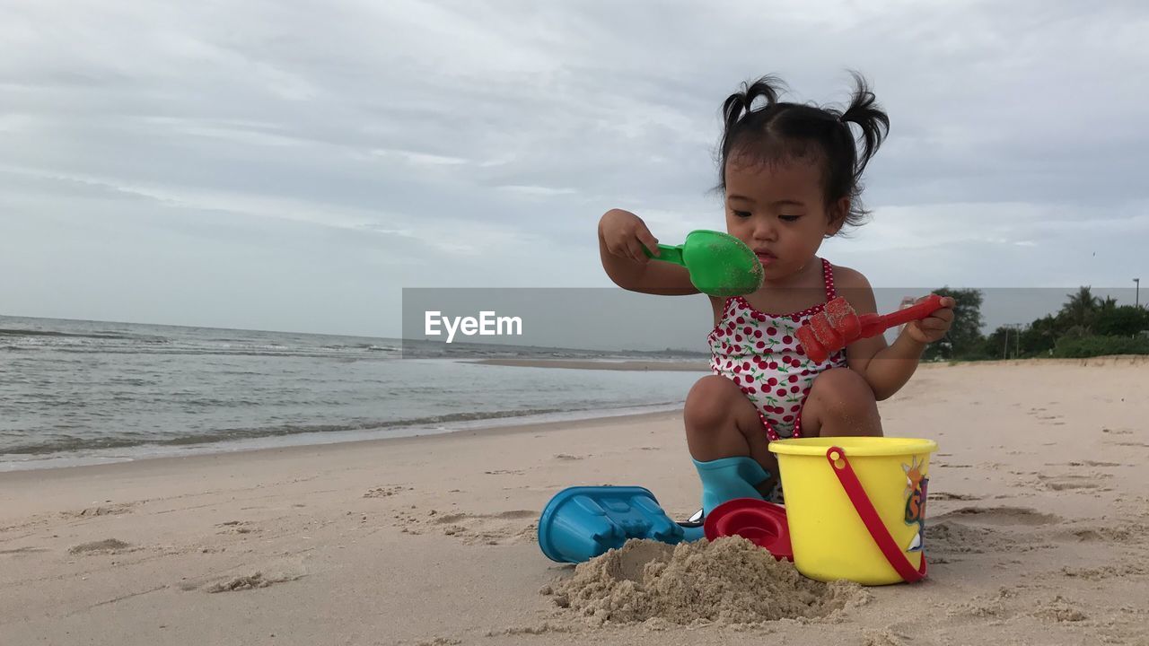 Cute girl playing on sand at beach against sky