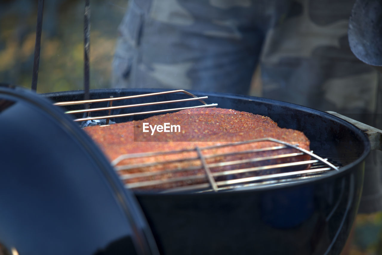 Midsection of man cooking beef on barbecue grill in yard