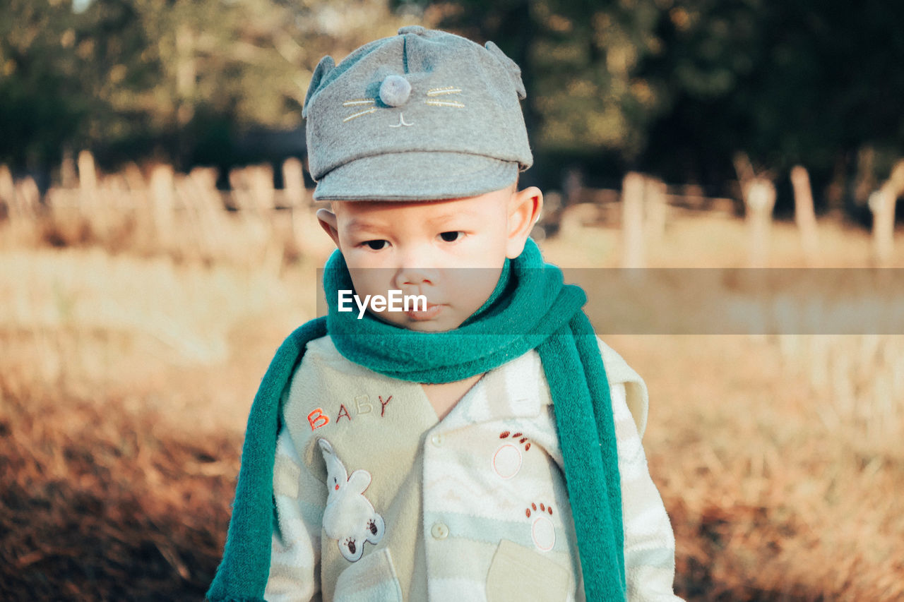 Cute baby boy wearing warm clothing and cap on land