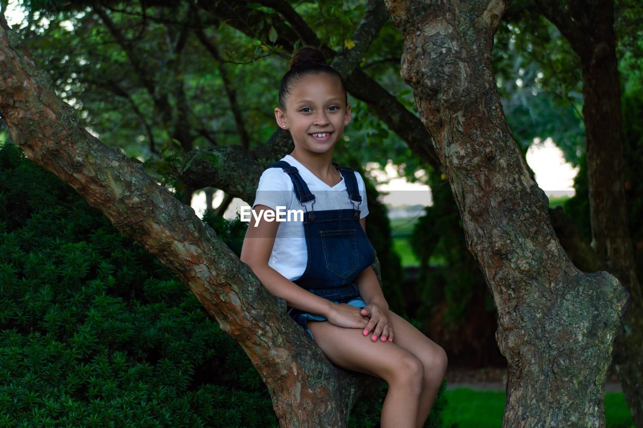 Portrait of smiling girl sitting on tree trunk