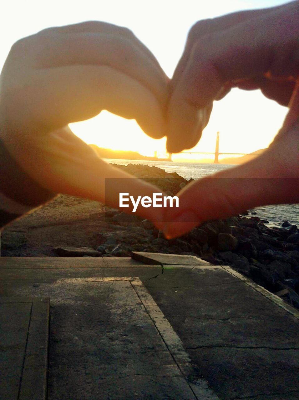 Cropped image of person forming heart shape during sunset