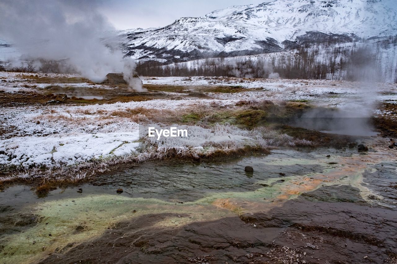 Smoke emitting from geyser against snowcapped mountains