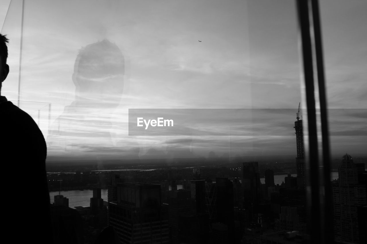 BUILDINGS IN CITY AGAINST SKY SEEN THROUGH GLASS WINDOW